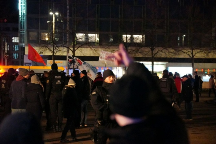 Personen mit Flaggen auf der Straße, davor Polizei