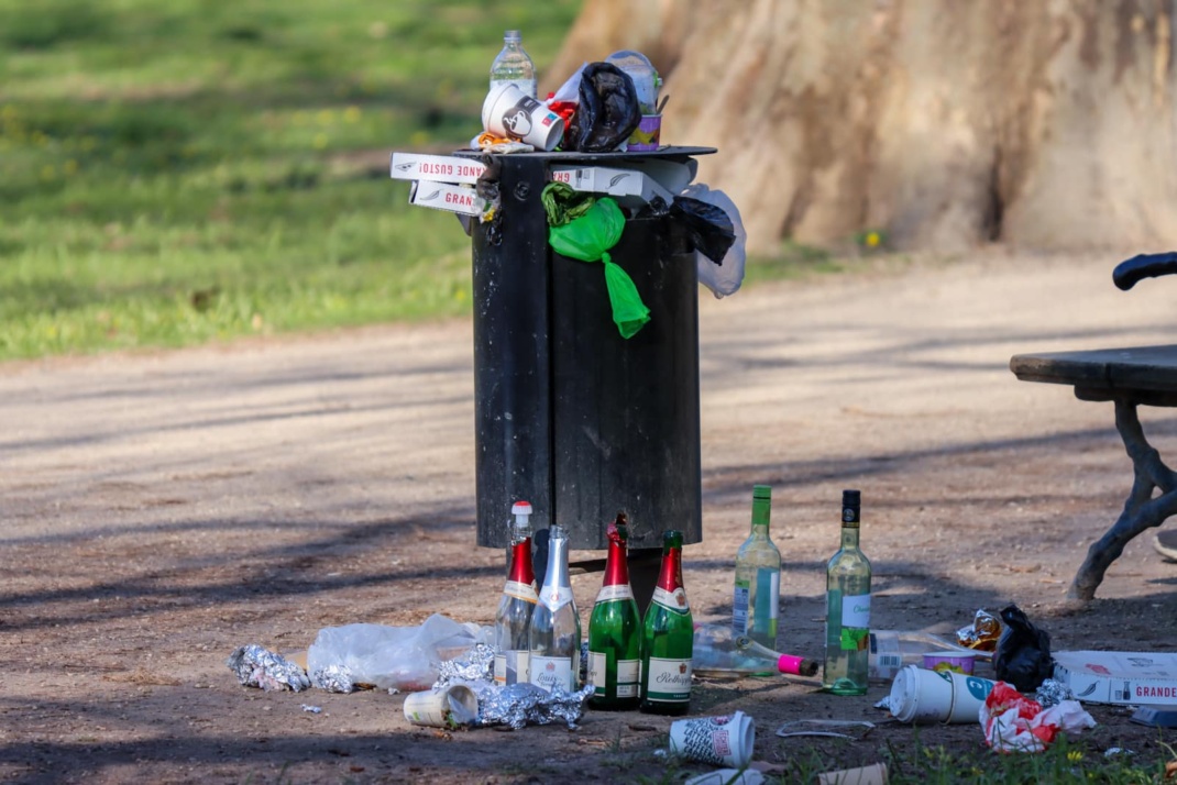 Ein übervoller Mülleimer im Park, Müll liegt auch drumherum auf dem Boden