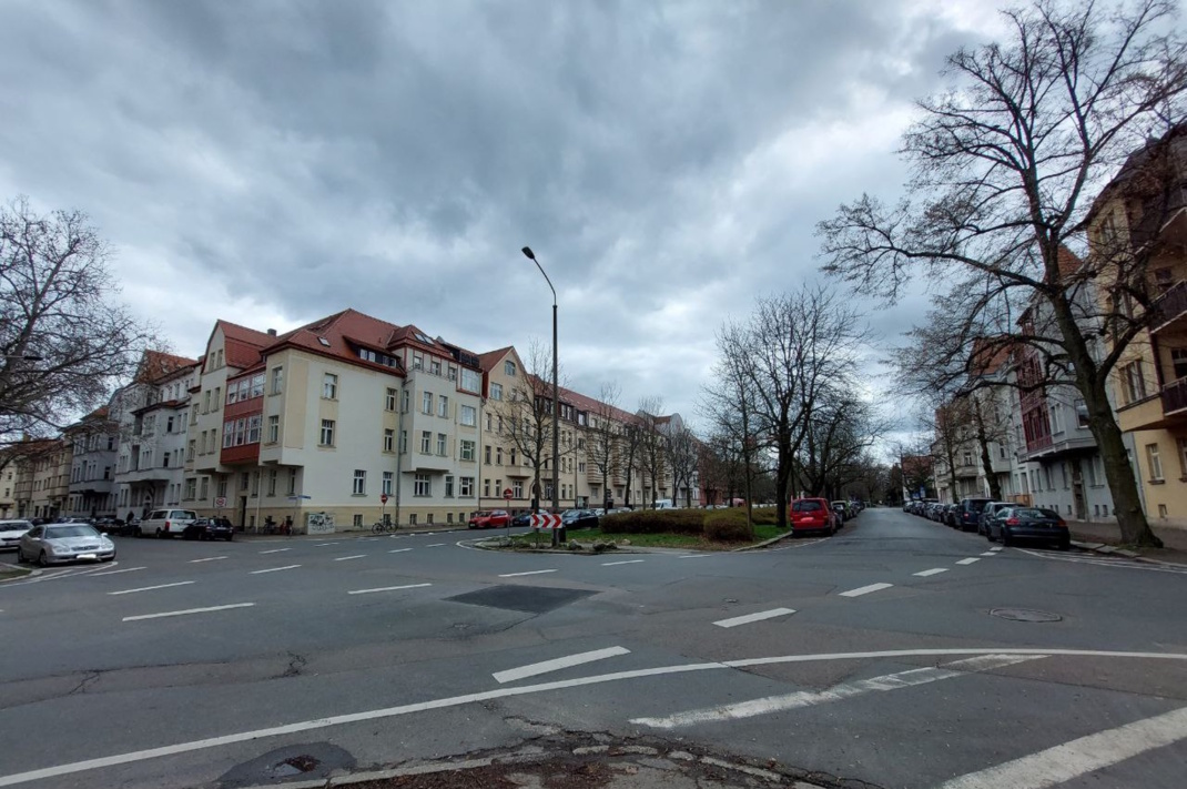 Straßenkreuzung in Leipzig, freie Fahrbahn, Bäume und Wohnhäuser.