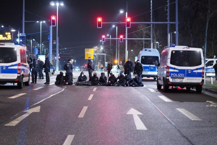 Personen sitzen auf der Straße, flankiert von Polizeiautos