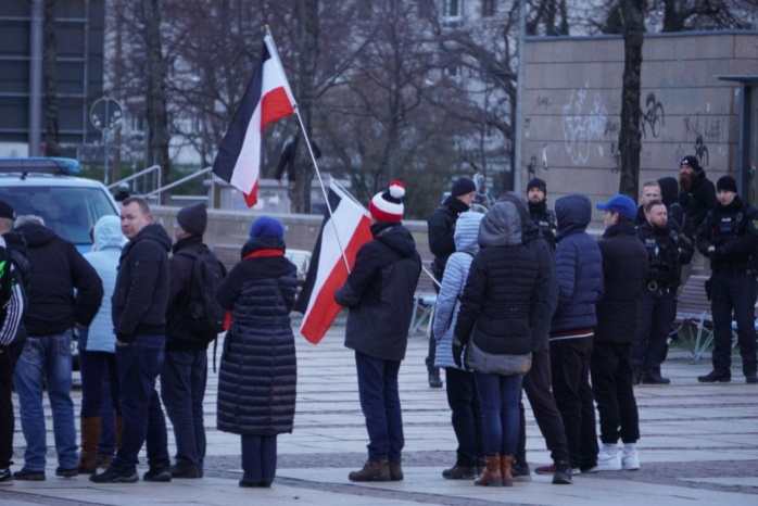 Eine Gruppe von Personen, mehrere schwarz-rot-weiße Flaggen sind zu serhen