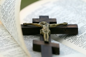 Ein Holzkreuz mit einer Jesusfigur liegt auf einer aufgeschlagenen Bibel.