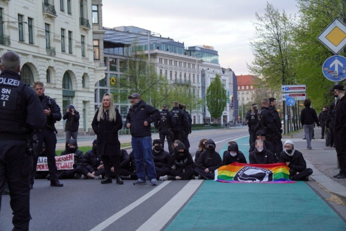 Personengruppe, schwarz gekleidet und mit bunten Fahnen, sitzt auf einer Straße