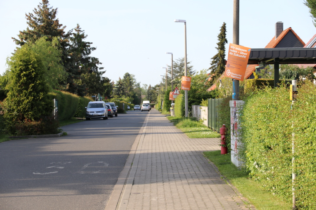 Kleine Straße mit Häusern, Hecken und Autos.