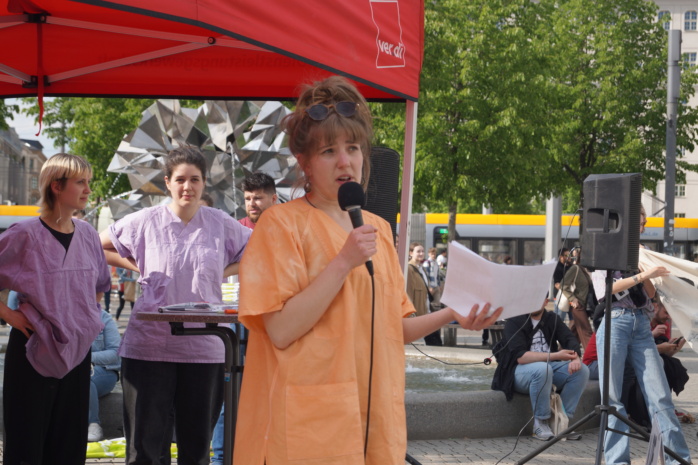 Eine Person in Kleidung aus dem Gesundheitswesen hält einen Redebeitrag auf einer Demonstration.