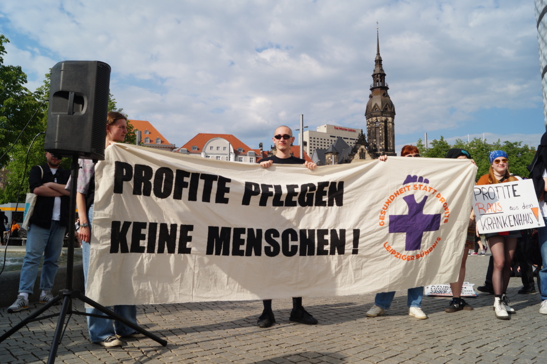 Personen halten ein Banner mit der Aufschrift "Profite pflegen keine Menschen!" hoch.