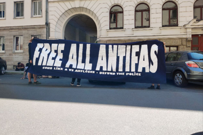Personen verdeckt hinter einem schwarzen Banner mit der Aufschrift "Free all Antifas"