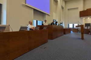 Ein Podium, daran sitzen vier Menschen, im Hintergrund ist ein großer Bildschirm zu sehen