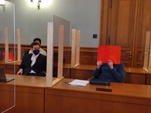 Angeklagter, Gesicht hinter roter Mappe, mit Anwalt im Gerichtssaal.