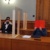 Angeklagter, Gesicht hinter roter Mappe, mit Anwalt im Gerichtssaal.