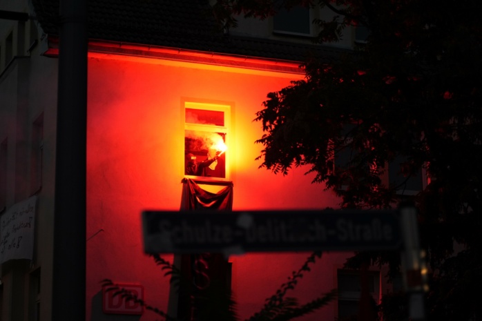 Aus einem Fenster wird rot brennende Pyrotechnik gehalten.
