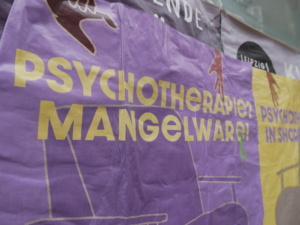 Lila Plakat mit gelber Aufschrift "Psychotherapie Mangelware"