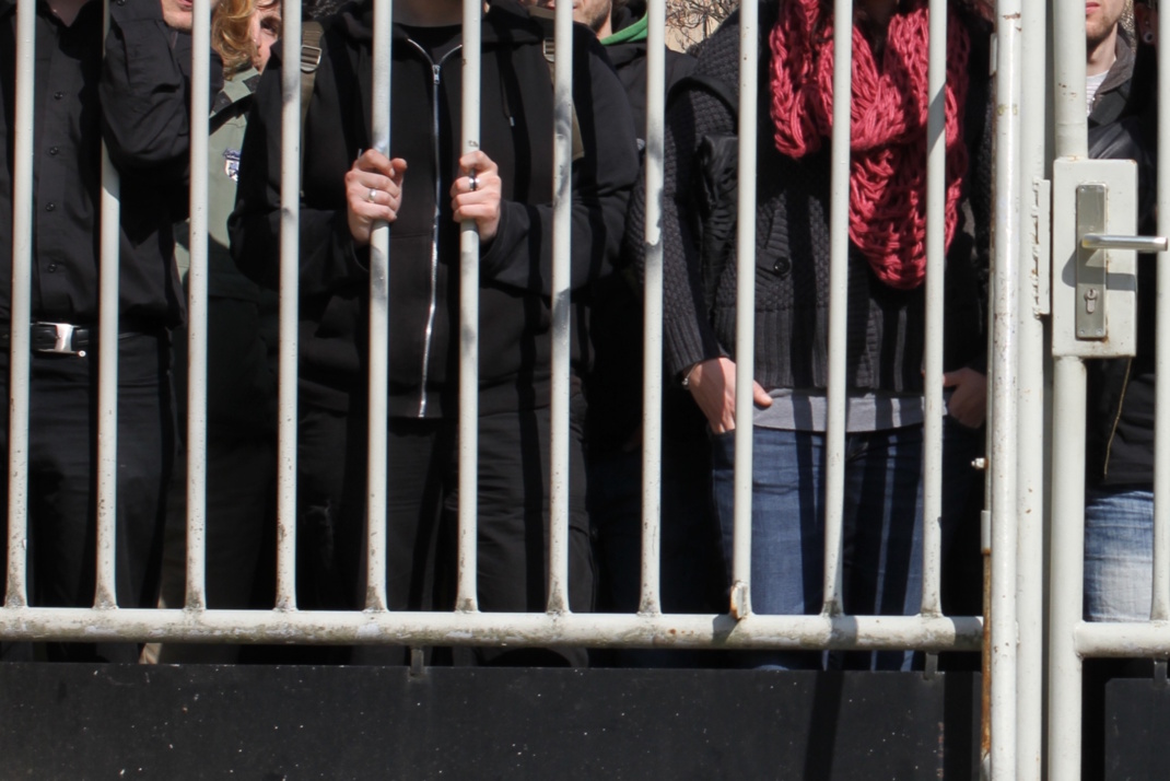 Personen hinter vergittertem Zaun.