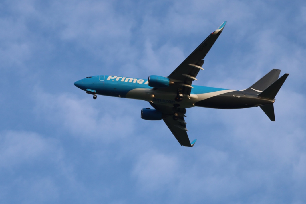 Frachtflugzeug vor blauem Himmel und Wolken von unten.