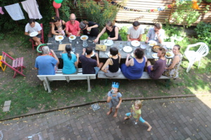 Menschen sitzen im Garten an einem Tisch zum essen.