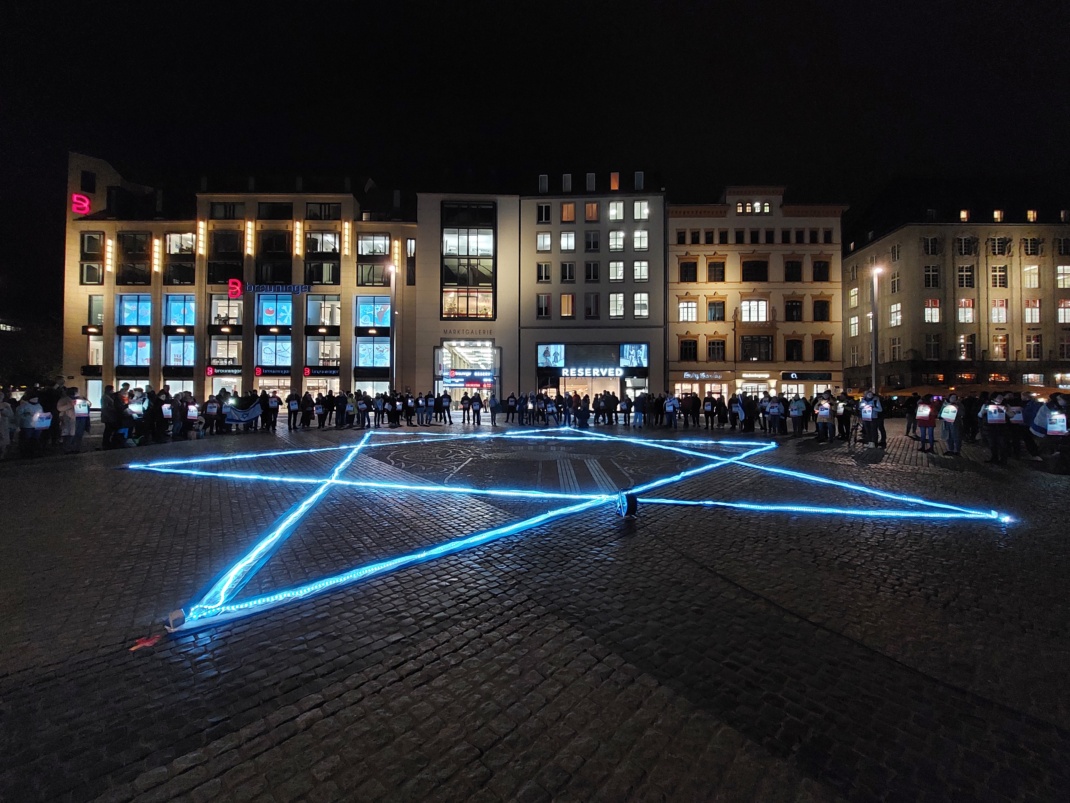 Beleuchteter Davidstern auf dem Grund und Menschen drumherum.