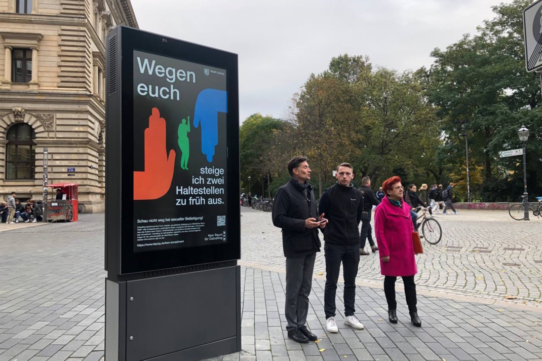 Plakat in den Innenstadt und drei Personen daneben.