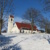 Kirche auf Hügel, blauer Himmel und kahle Bäume im Schnee.