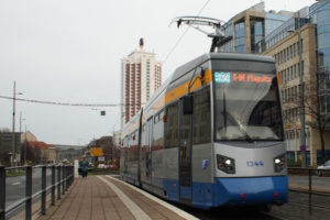 Tram an Haltestelle, Messe-Hochhaus und Gebäude an der Seite.