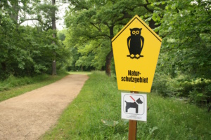 Bäume, Sträucher und gelbes Naturschutz-Schild.