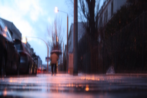 Verschwommenes Bild, Fußweg, Regen und Person mit Schirm auf der Straße unterwegs,