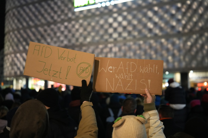 Zwei Personen halten Demo-Schilder hoch in einer Menschenmenge