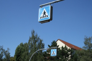Markierungsschilder zum Fußgängerüberweg an Pfahl, blauer Himmel.