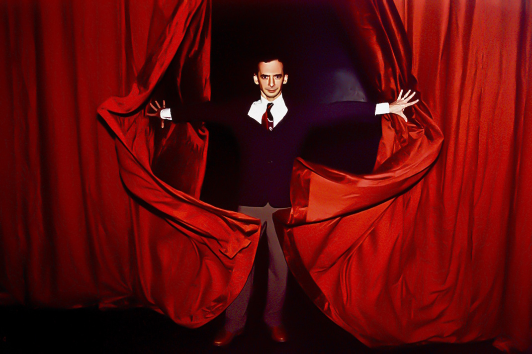 Männliche Person tritt hinter rotem Vorhang hervor.
