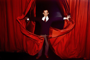 Männliche Person tritt hinter rotem Vorhang hervor.