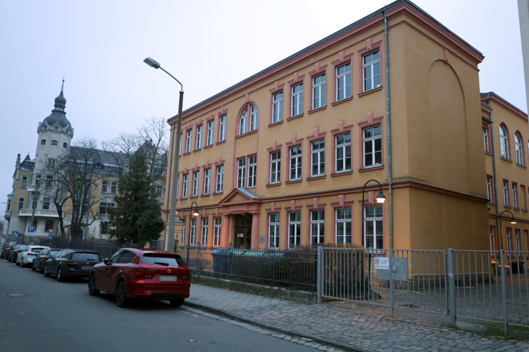 Schulgebäude von außen, Straße und geparkte Autos.