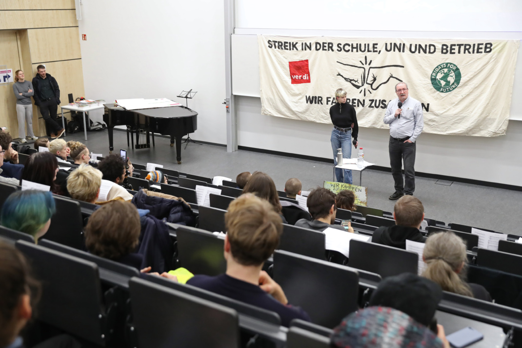 Hörsaal, Personen auf der Bühne, Transparent.