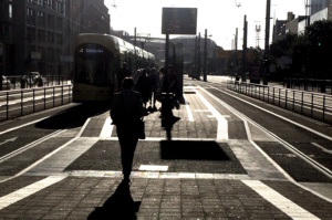 Tramhaltestelle, Plattform, Straßenbahn und Personen schemenhaft im Gegenlicht.