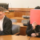 Angeklagter hält Gesicht mir rotem Ordner bedeckt, daneben sein Anwalt.