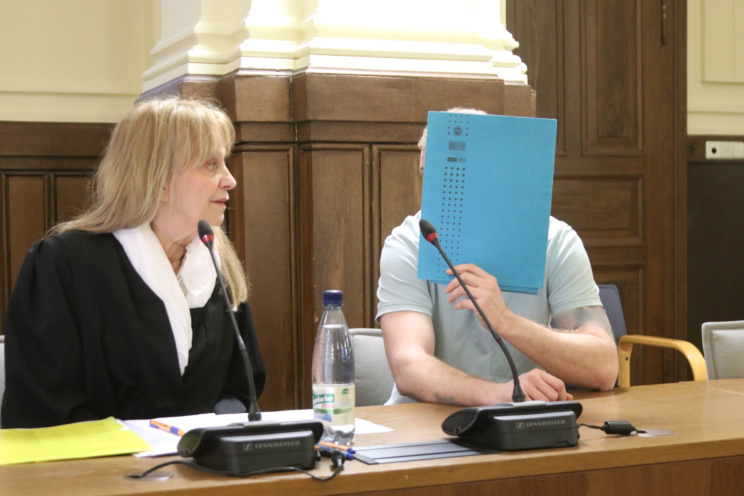 Angeklagter, der sich eine Mappe vors Gesicht hält, mit einer Verteidigerin.