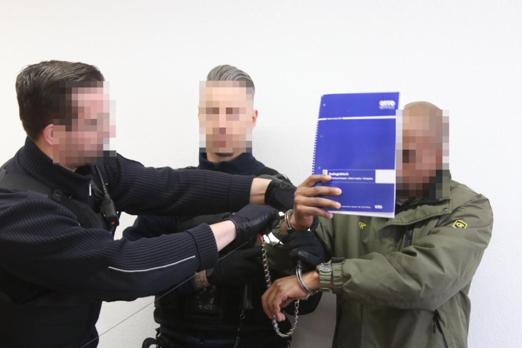 Abnahme der Handschellen bei einem Mann im Gerichtssaal durch zwei Wachtmeister,