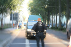 Polizeibeamter in Uniform steht vor einem Wagen auf der Straße, verschwommenes Bild von hinten.