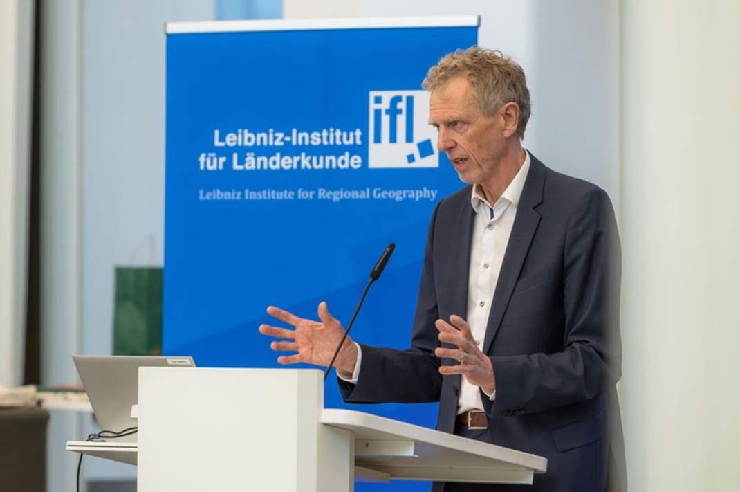 Mann am Rednerpult, Hände gestikulierend.