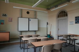Klassenzimmer mit Tafel, Tischen und Stühlen.