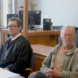 Angeklagter und Anwalt in Robe sitzen im Gerichtssaal.