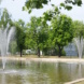 Wasserbecken mit Fontänen, umgeben von Bäumen.