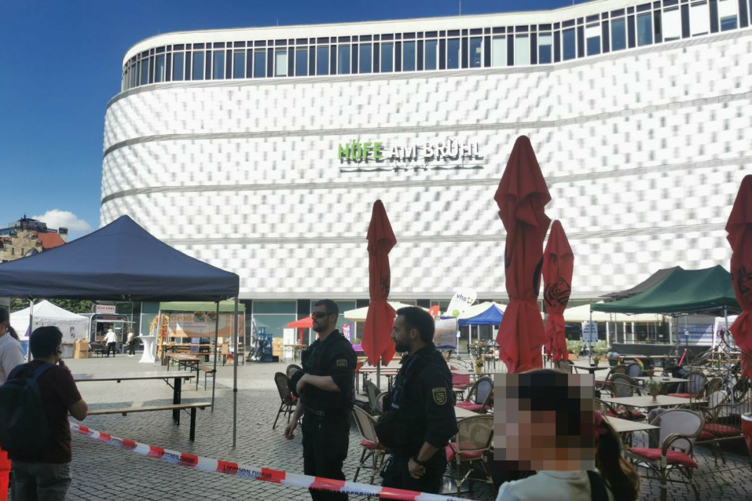 Absperrband mit bewachenden Polizistenn und Menschen an öffentlichem Platz,