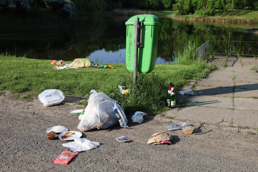 Öffentlicher Müllbehälter und Abfälle daneben.