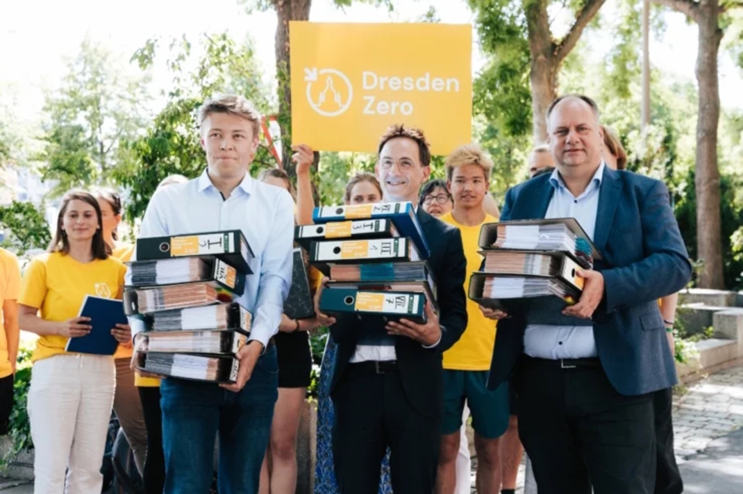 Gruppe von Personen, teilweise gestapelte Aktenordner haltend.