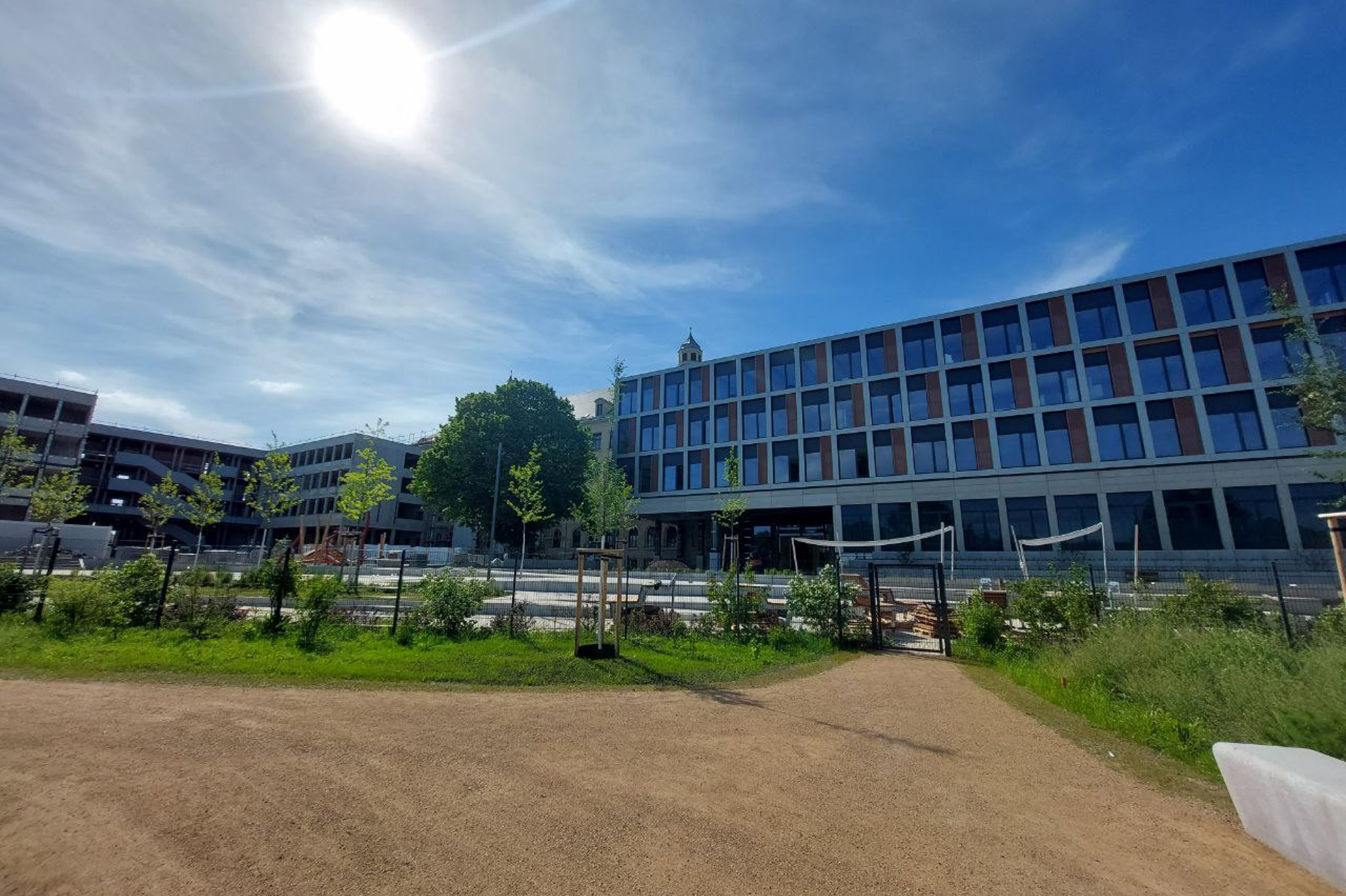Schulcampus mit Hof, blauer Himmel und Sonne.