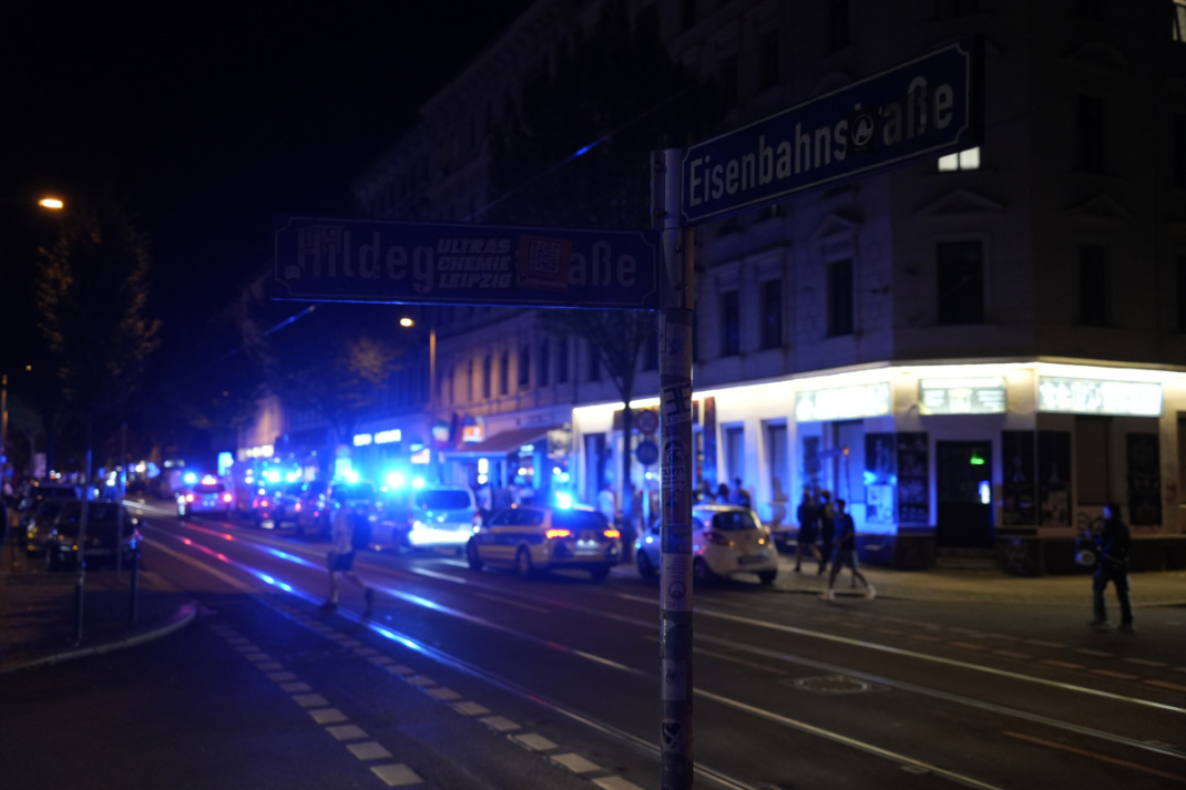 Straßenschild, Einsatzfahrzeuge mit Blaulicht in der Dunkelheit.