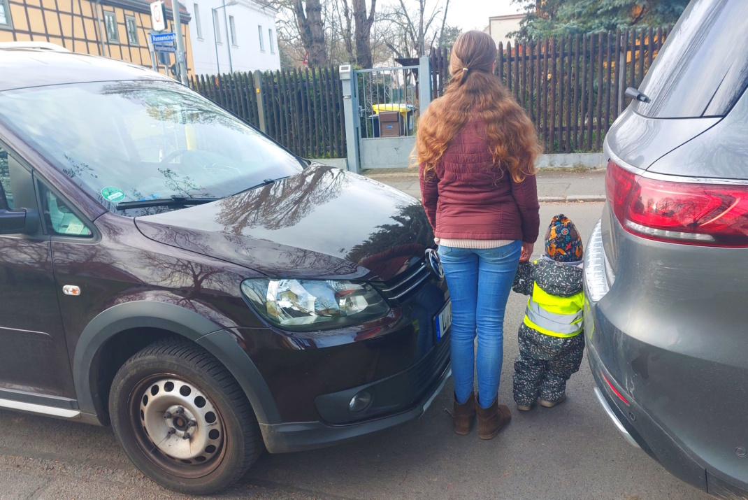 Mutter steht mit kleinem Kind in enger Parklücke zwischen zwei PKW.