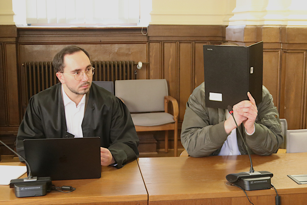 Angeklagter, der sein Gesicht verbirgt, sitzt neben seinem Anwalt im Gerichtssaal.