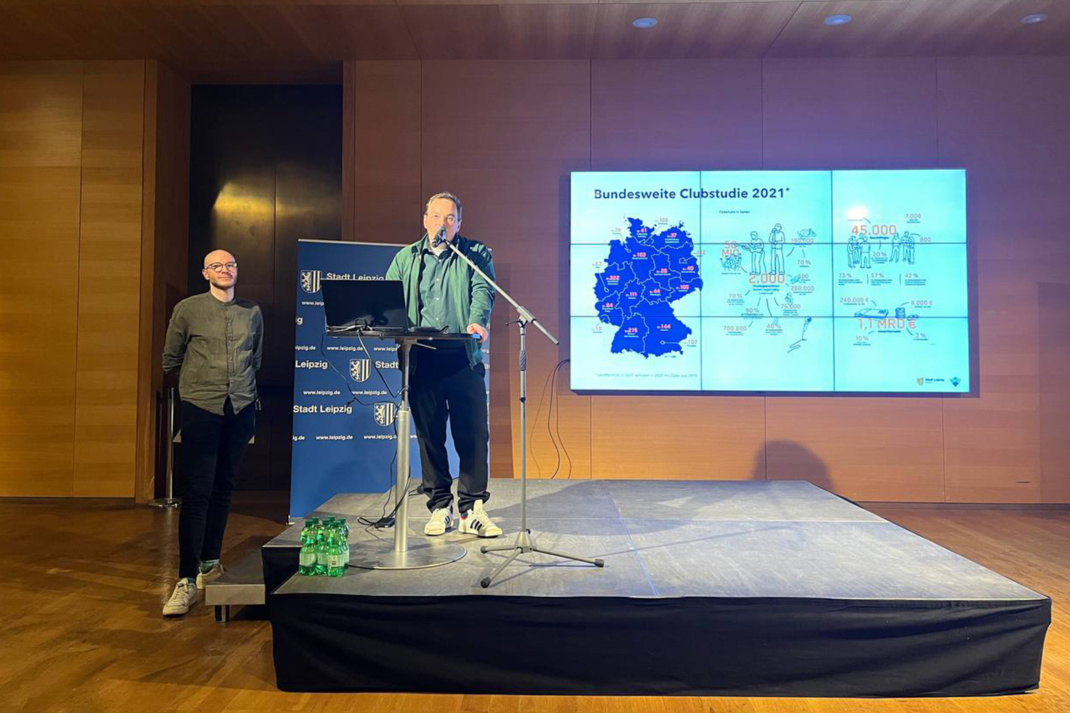 Bühnenpräsentation, ein Vortragender steht vor einem Bildschirm.