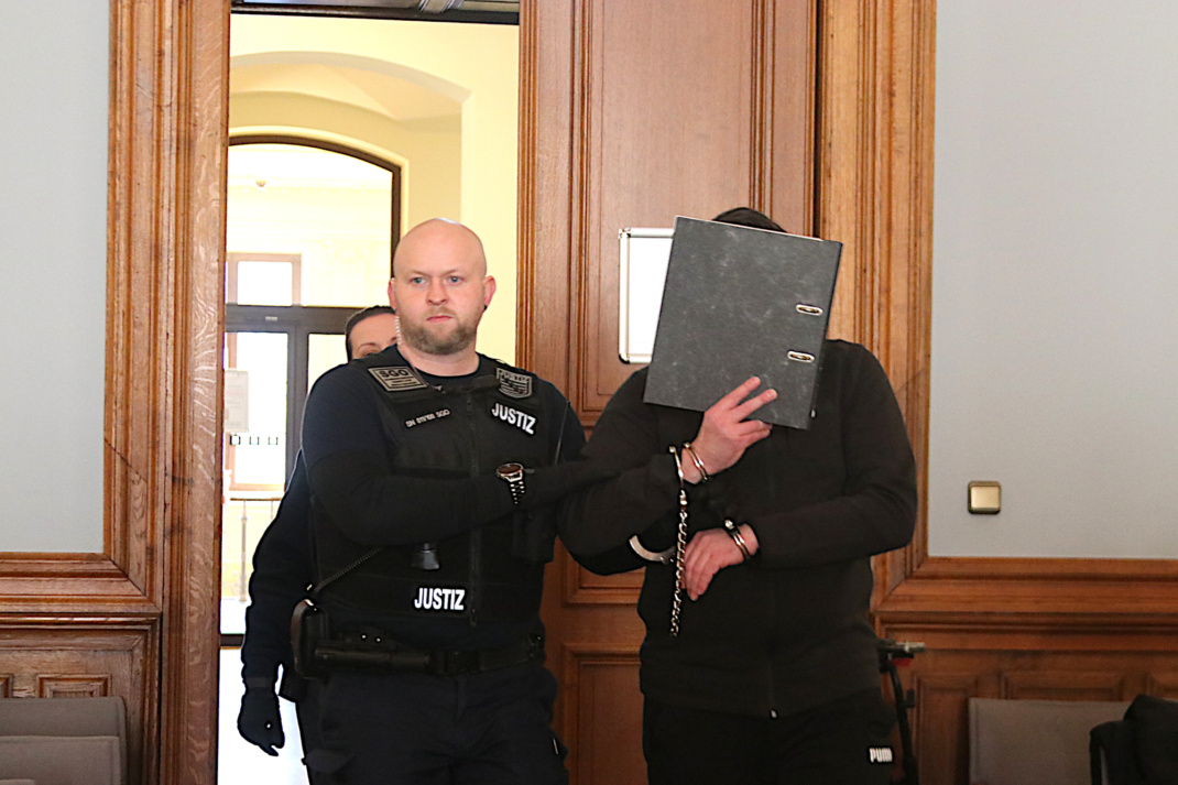 Angeklagter wird von Justizbeamten hereingebracht in den Verhandlungssaal.