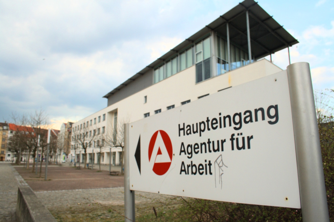 Wegweiser zur Agentur für Arbeit, Gebäude im HIntergrund.